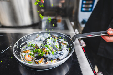 chef cooks mussels in a pan, garnishing with herbs