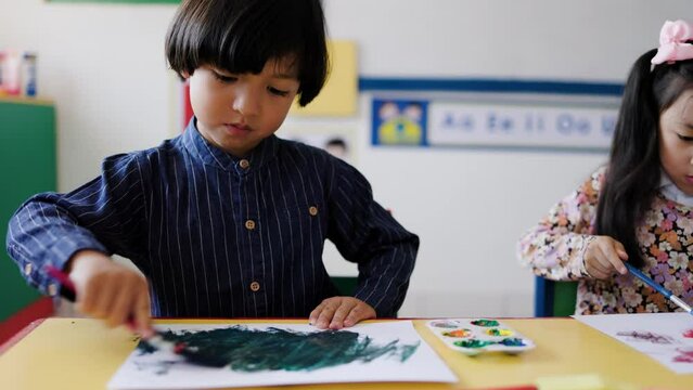 Asian kid painting during art class in kindergarten class room. Multiracial children students and school education