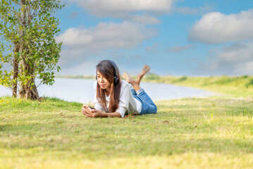 Girl enjoy listening music and reading a book and play laptop on the grass field of the park in the...