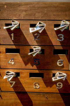 A vertical array of wooden mailboxes with numbers from 1 to 9, each containing rolled-up newspapers.