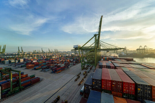Sunrise over a bustling container port, showcasing rows of colorful shipping containers, towering cranes, and the vast infrastructure necessary for marine cargo operations.