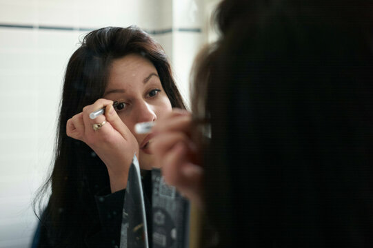 A woman is applying mascara to her eyelashes while looking into a mirror.