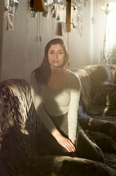 A woman sitting on a sofa in a sunlit room, surrounded by hanging photographs.