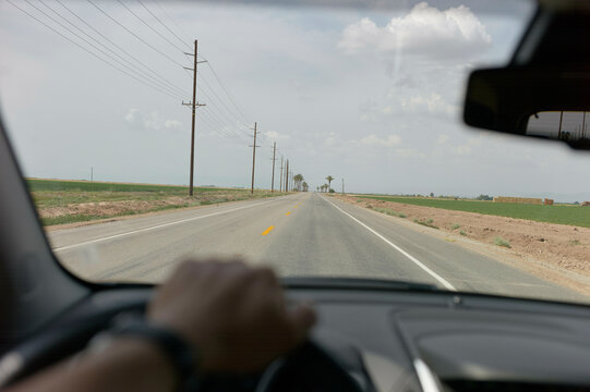 A view from the driver's perspective inside a car traveling down a straight road lined with utility poles under a cloudy sky.