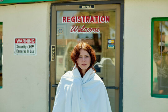 A person wrapped in a white blanket stands in front of a building with a sign saying \REGISTRATION Welcome\"."
