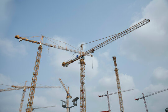 A cluster of construction cranes towers against a cloudy sky, indicating a large-scale building project.