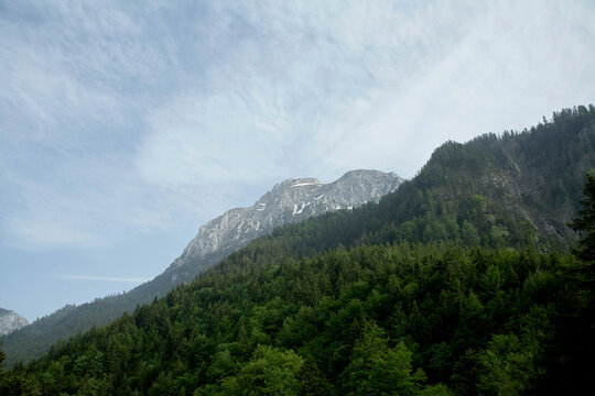A picturesque view of a mountain peak rising above a lush green forest under a sky streaked with wispy clouds.