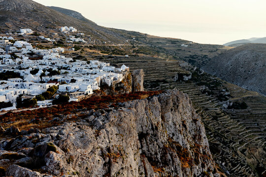A scenic view of a traditional white village nestled in rugged hills, bathed in the warm glow of the setting sun.