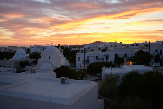 Sunset over a serene town with buildings displaying the iconic whitewashed architecture under a dramatic sky.