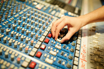 A hand adjusting a knob on a professional audio mixing console with numerous buttons and sliders. 