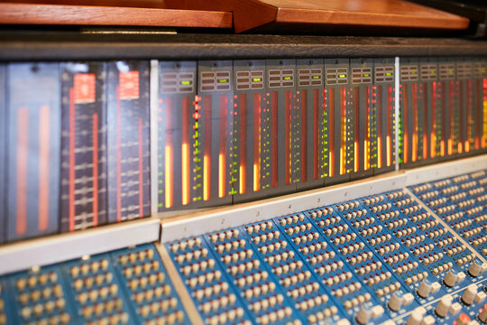 Close-up view of a professional audio mixing console with faders and adjustable knobs, the LED level meters are lit indicating active sound levels.