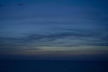 A calm ocean horizon under a twilight sky with subtle gradients from deep blue to orange near the horizon, and streaks of clouds above.