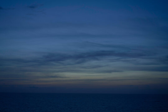 A calm ocean horizon under a twilight sky with subtle gradients from deep blue to orange near the horizon, and streaks of clouds above.