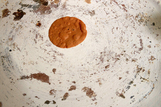 A single, freshly-baked chocolate chip cookie sits in the center of a well-used, aged baking sheet with bits of cookie residue around it.