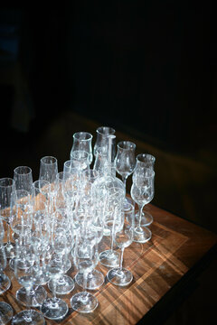 A collection of clean, empty glassware is arranged on a wooden surface, illuminated by a beam of natural light against a dark background.