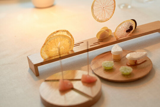 An elegant dessert presentation featuring thinly sliced citrus fruit and various sweets artistically displayed on wooden stands with a warm, diffused lighting.