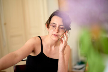 A person with glasses is captured indoors holding a cellphone to their ear, seemingly engaged in a conversation.
