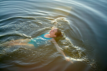A young woman is swimming in calm water with sun rays reflecting on the surface.