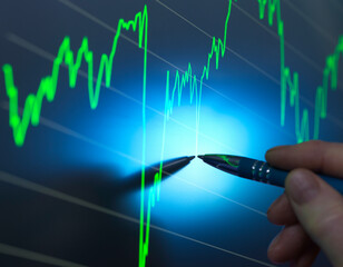 A person's hand holding a pen points to a peak in a glowing stock market graph on a digital screen, indicating a significant increase in values.