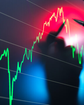 A blurred silhouette of a person is seen in the foreground with a background of a stock market chart displaying a fluctuating trend line in red and green.