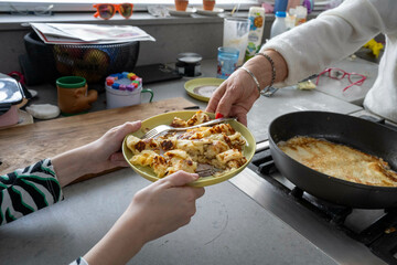Two people share a plate of freshly cooked crepes at a kitchen counter with various cooking items and utensils around.