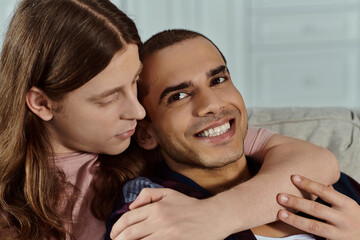 a gay couple, in casual clothes happily hugging on a cozy couch at home.