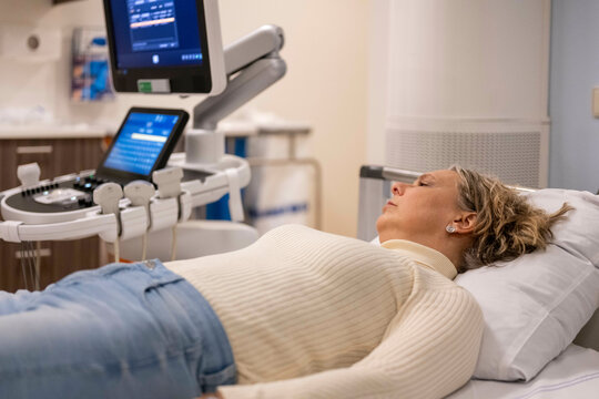 A woman lies on a medical examination table next to an ultrasound machine, appearing calm and awaiting a procedure.