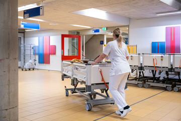 A healthcare worker in white uniform is pushing a cart in a hospital hallway featuring colorful wall accents and directional signs.