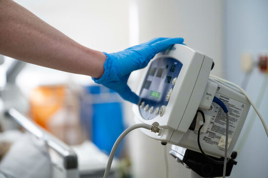 A gloved hand adjusts settings on a medical device with a digital screen, suggesting a healthcare setting. - Powered by Adobe