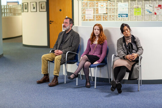 Three people sitting on chairs in a waiting area of a medical practice