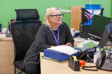Woman smiling at work with computer and papers in the office of a medical practice