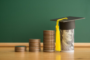 US dollars banknote wears graduation cap, stack coins chalkboard background. Education expense...