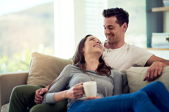 Couple, drinking coffee and laugh in home living room, talking or bonding together to relax. Tea cup, happy man and woman in funny conversation on sofa for healthy relationship, connection or support - Powered by Adobe