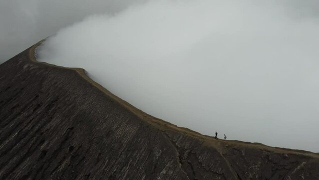 Two people walking on the Bromo volcano crater while it's smoking in Java, Indonesia, drone rotating around them
