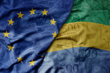 big waving realistic national colorful flag of european union and national flag of gabon on a euro money banknotes background.