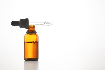 Black cap with pipette lies on open brown glass bottle.