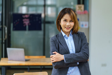 Confident young Asian businesswoman keeping her arms crossed and looking at the camera while...