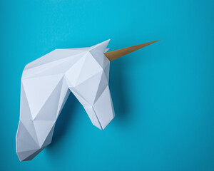 White 3d papercraft model of unicorn head on blue background. Minimal art concept.