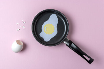 Paper fried egg in small frying pan on pastel pink background. Minimal food concept.
