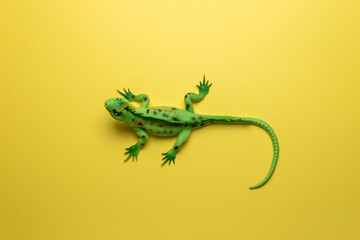 Green lizard toy on bright yellow background. Minimal art concept.