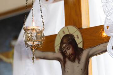 Burning candle against wooden cross with Jesus Christ. Selective focus.