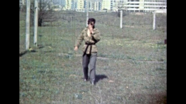 Caucasian Man in Karate kimono running by green grass, on sunny summer nature backdrop. Confident person karateka walking in natural city landscape background. Vintage color film. Retro 1980s archive