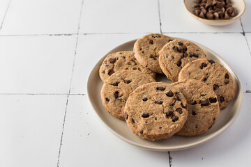 Plate of chocolate chip cookies with extra chocolate chips on side, set on a tiled background