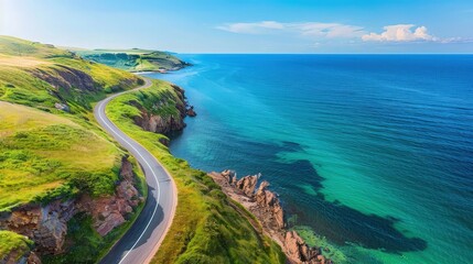 Overhead view of a winding coastal road with vibrant green cliffs on one side and a deep blue sea on the other, under a clear azure sky. - Powered by Adobe