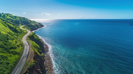 Overhead view of a winding coastal road with vibrant green cliffs on one side and a deep blue sea...