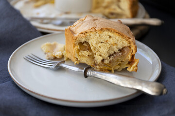 Piece of Apple sponge cake on a light colored plate with vintage fork on dark background, close-up side view food photography