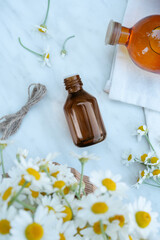 Bottle of essential oil and chamomiles on a light table.Top view ,flat lay. Space for text.     