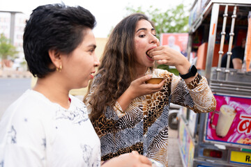 Two Young indian girls eating Pani puri, golgappa on roadside. Two Friends enjoying, exploring traditional Indian street food. Foodie, delicacies, culinary, snack concept