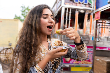 Young indian woman eating Pani puri, golgappa on roadside street food stall. Foodie, delicacies,...