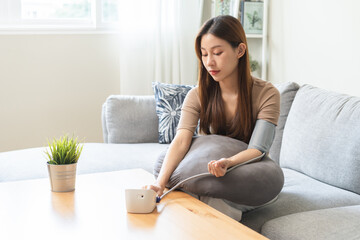Hypotension, asian young woman sitting on couch checking blood high pressure and heart rate with...
